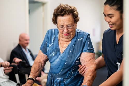 Female healthcare worker assisting an elderly woman on rollator walker indoors - Australian Stock Image