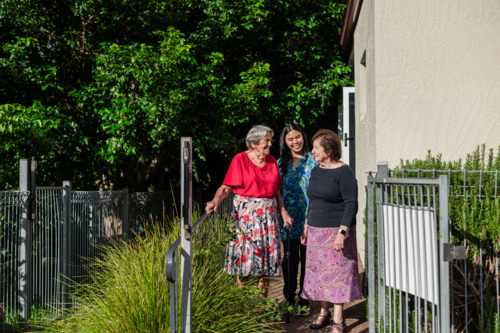 Female healthcare worker assisting two elderly women for a walk on a paved path outdoors - Australian Stock Image