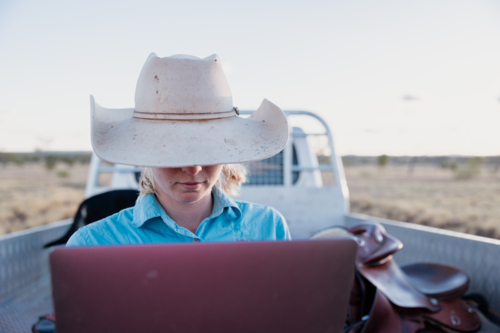 Female looking at computer outdoors with vehicle in background - Australian Stock Image