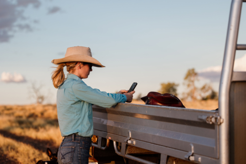 Female looking at phone leaning on farm vehicle - Australian Stock Image