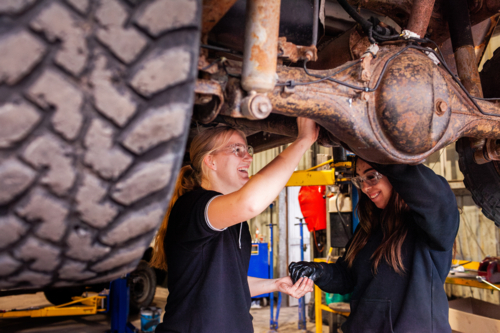 female mechanic tradeswomen working on car repair together in industrial workshop - Australian Stock Image