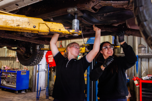 female mechanic tradeswomen working together on car repair in industrial workshop - Australian Stock Image