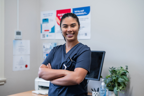 Female nurse in blue scrubs standing inside the clinic with her arms crossed - Australian Stock Image