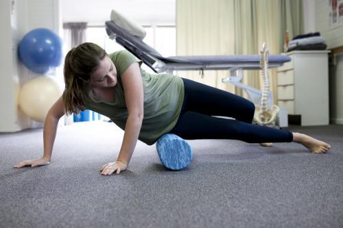 Female patient using a foam roller in a physio studio - Australian Stock Image