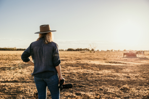 Female photographer facing away holding camera on farm - Australian Stock Image