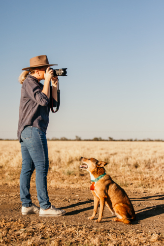 Female photographer outdoors looking through camera with dog - Australian Stock Image