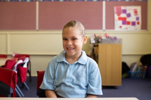 Female primary school student sitting smiling in a classroom - Australian Stock Image