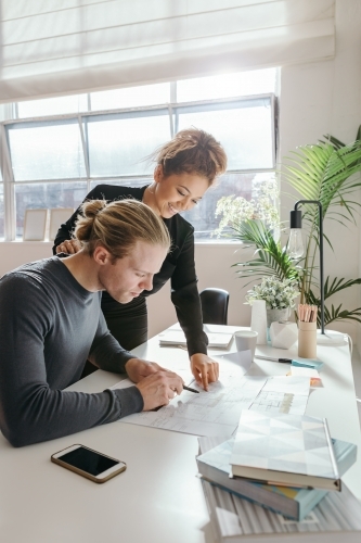 Female professional looking over the plans of a co-worker - Australian Stock Image