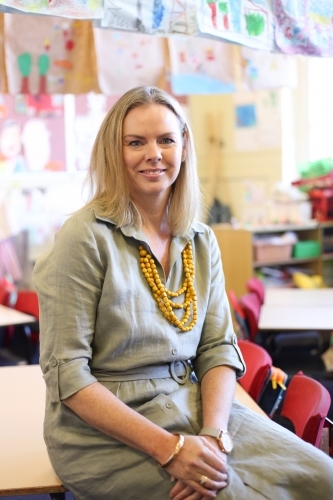 Female school teacher sitting on a classroom desk - Australian Stock Image
