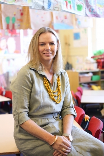 Female school teacher sitting on a classroom desk