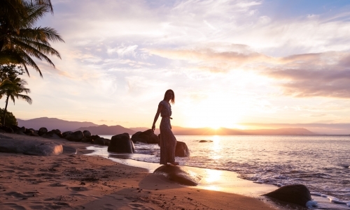 Female standing on rock at the beach with sunset skies