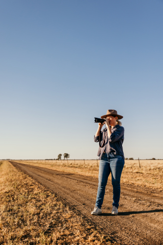 Female standing on rural dirt road taking photo - Australian Stock Image