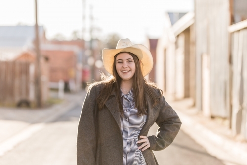Female teen wearing hat standing with hand on hip smiling - Australian Stock Image