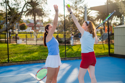 Female tennis player coaches another female into serving a tennis ball - Australian Stock Image