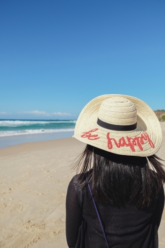 Female wearing be happy hat on the beach - Australian Stock Image