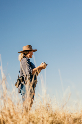 Female with camera over shoulder flying a drone looking to the sky - Australian Stock Image