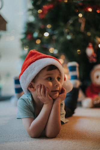 Festive young boy enjoys the holiday season wearing santa hat by tree - Australian Stock Image