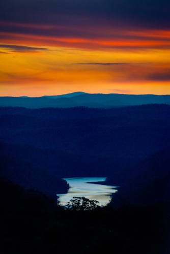Fiery sunset over layered mountain ridges with a winding river glowing below. - Australian Stock Image