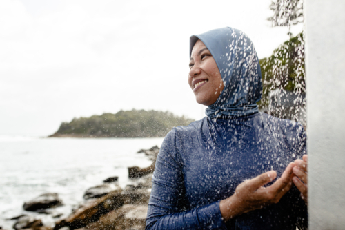 Filipina woman in a light blue headscarf standing beneath an outdoor shower - Australian Stock Image
