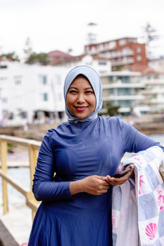 Filipina woman walking on coastal path holding a phone and a towel on the other hand - Australian Stock Image