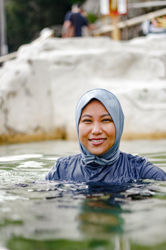Filipina woman wearing light blue headscarf submerged in a clear tidal pool - Australian Stock Image