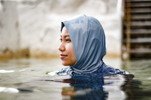Filipina woman wearing light blue headscarf submerged in a clear tidal pool - Australian Stock Image
