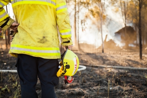 Fire fighter standing beside burnt grass holding safety helmet in hand