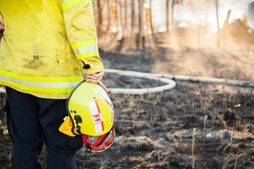 Fire fighter standing beside burnt grass holding safety helmet in hand - Australian Stock Image