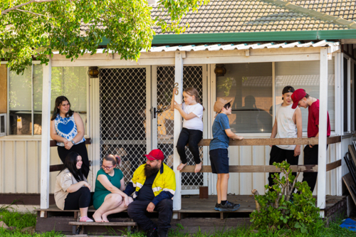 First nations Australian family with dad in workwear together on front porch of home - Australian Stock Image