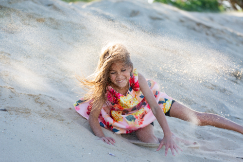 First Nations Australian Torres Strait Islander kid rolling down sand dune at the beach - Australian Stock Image