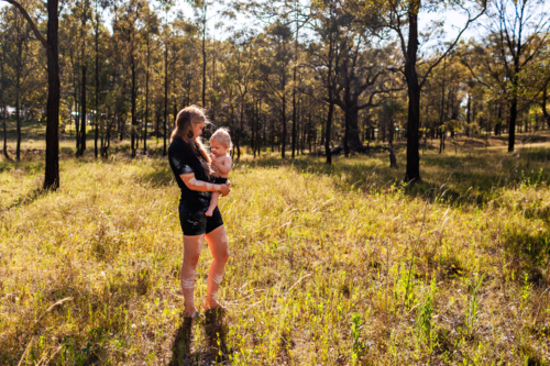 First nations Australian woman with baby boy walking in Australian paddock bushland - Australian Stock Image