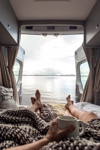 first person perspective of barefoot couple relaxing in a camping van with an ocean view