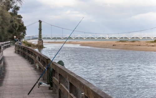 Fisherman at coastal river with bridge in background