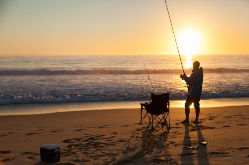 Fisherman fishing of beach at sunrise on clear morning - Australian Stock Image