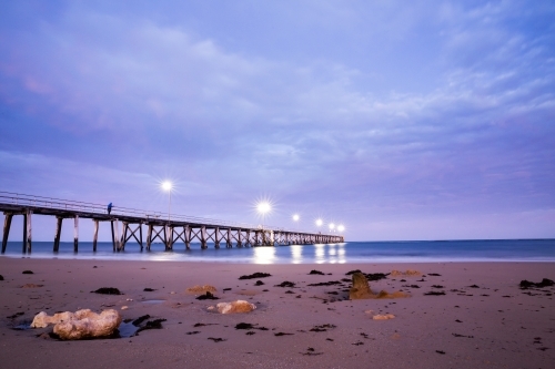 fisherman on jetty at dawn under cloudy sky - Australian Stock Image