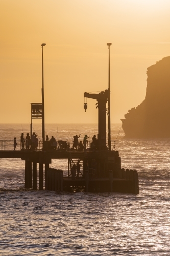 Fishermen and sightseers on a jetty in front of a golden sky - Australian Stock Image
