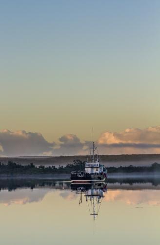 Fishing boat on calm waters with reflection - Australian Stock Image