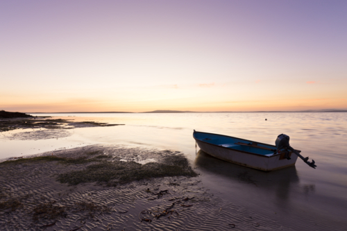 Fishing dinghy on the beach at low tide during calm sunset over the sea in South Australia - Australian Stock Image