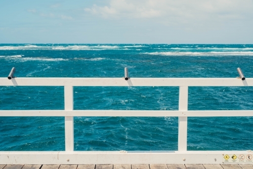 Fishing poles on a pier by the ocean - Australian Stock Image