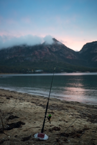 Fishing rod on beach at sunset with mountains and mist in background - Australian Stock Image