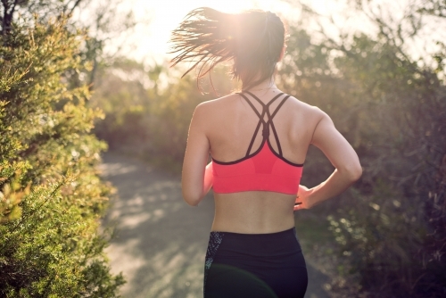 Fit Asian woman running for morning exercise, with lens flare - Australian Stock Image