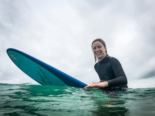 Fit, healthy natural woman sitting on longboard surfboard on overcast day - Australian Stock Image