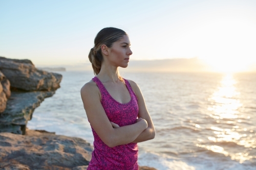 Fitness woman with standing on coastal headland at sunrise