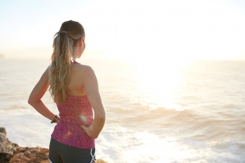 Fitness woman with standing on coastal headland at sunrise
