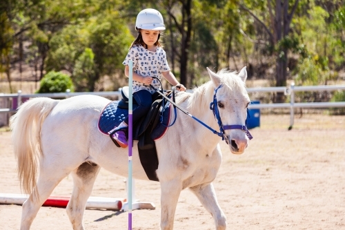 Five year old horse rider doing pole bending on white pony - Australian Stock Image