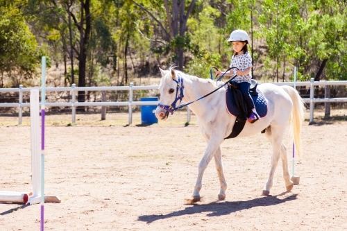 Five year old horse rider doing pole bending on white pony - Australian Stock Image
