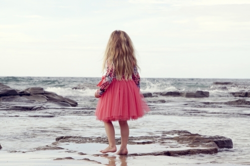 five year old walking along beach looking away