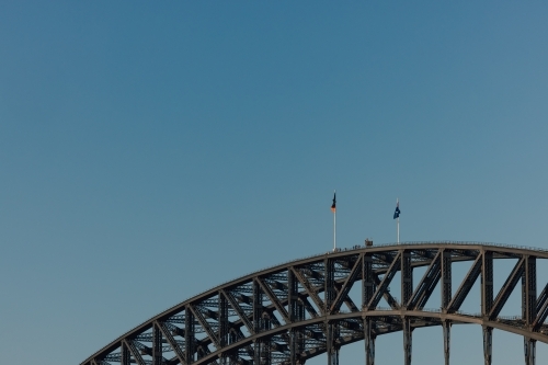Flags flying at the peak of the Sydney Harbour Bridge with group of people climbing - Australian Stock Image