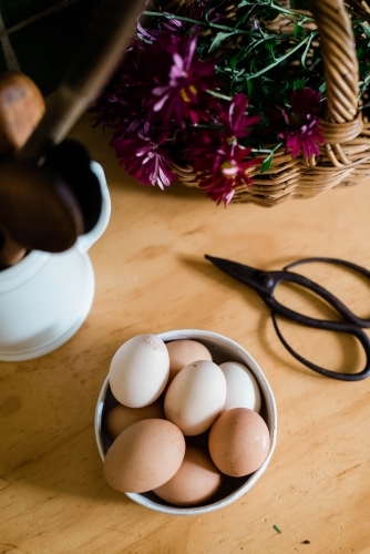 Flat lay of bowl of eggs, floral scissors, basket of flowers and cup of utensils