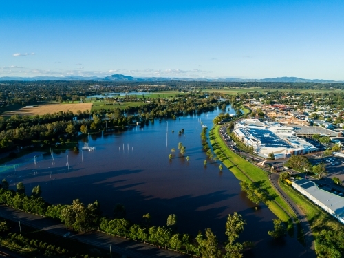 Flooded playing fields and park with floodwater rising up levee bank towards town and shops - Australian Stock Image